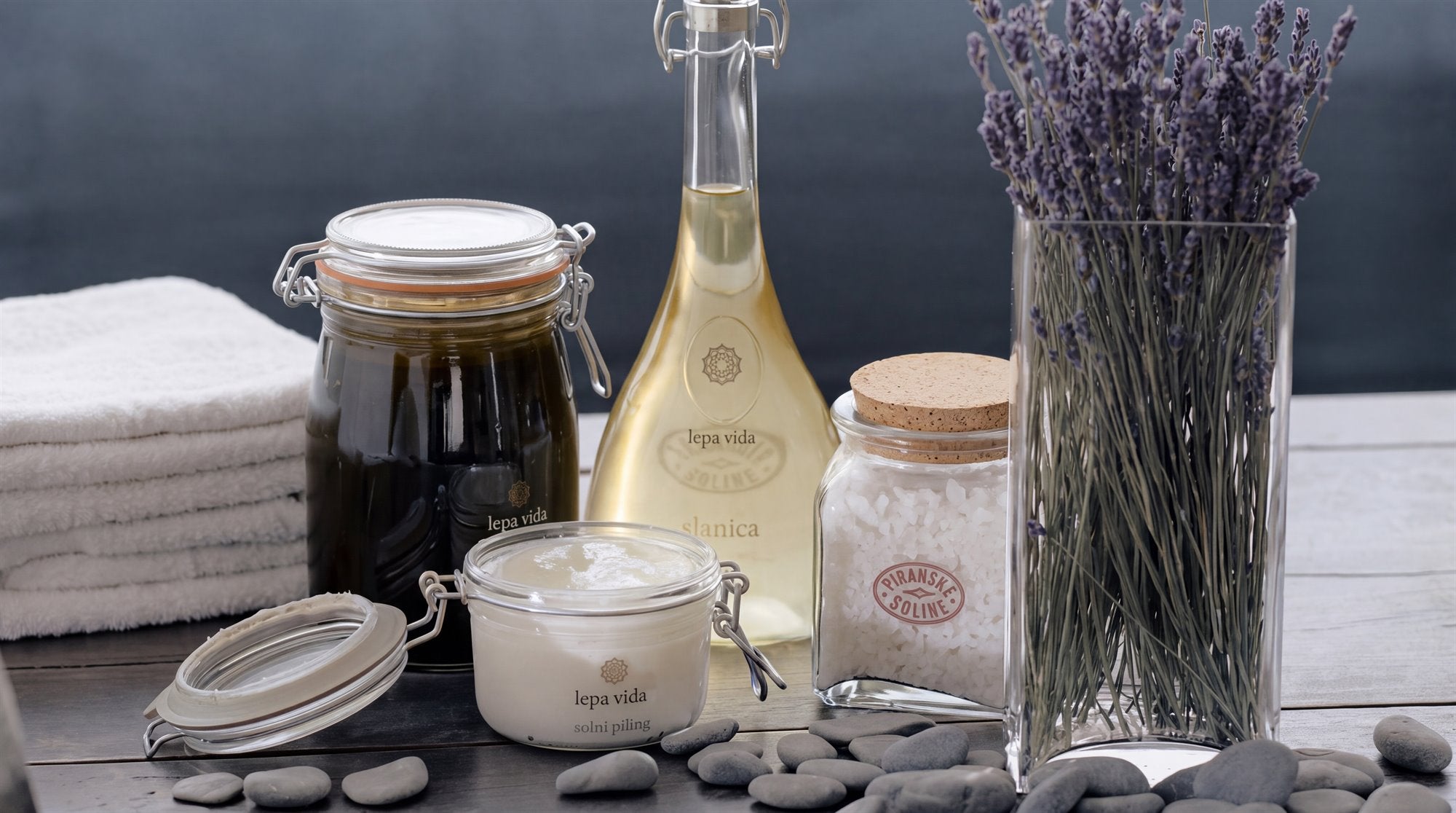 Pflegeprodukte der Reihe Lepa Vida auf einem Holztisch: Salzpeeling, Körperöl, Meersalz, Algenextrakt und getrockneter Lavendel